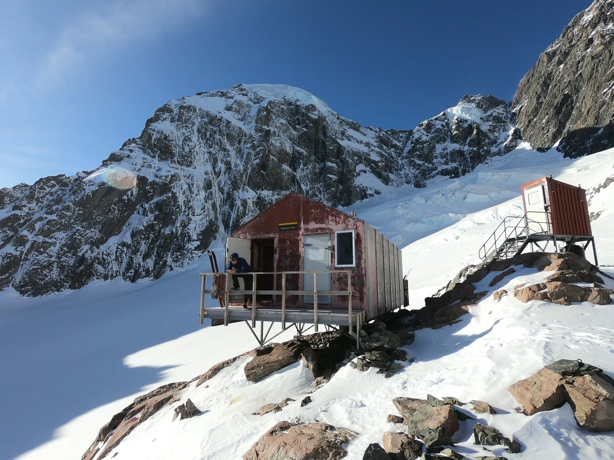 A small alpine hut on a rocky knoll surrounded by snow