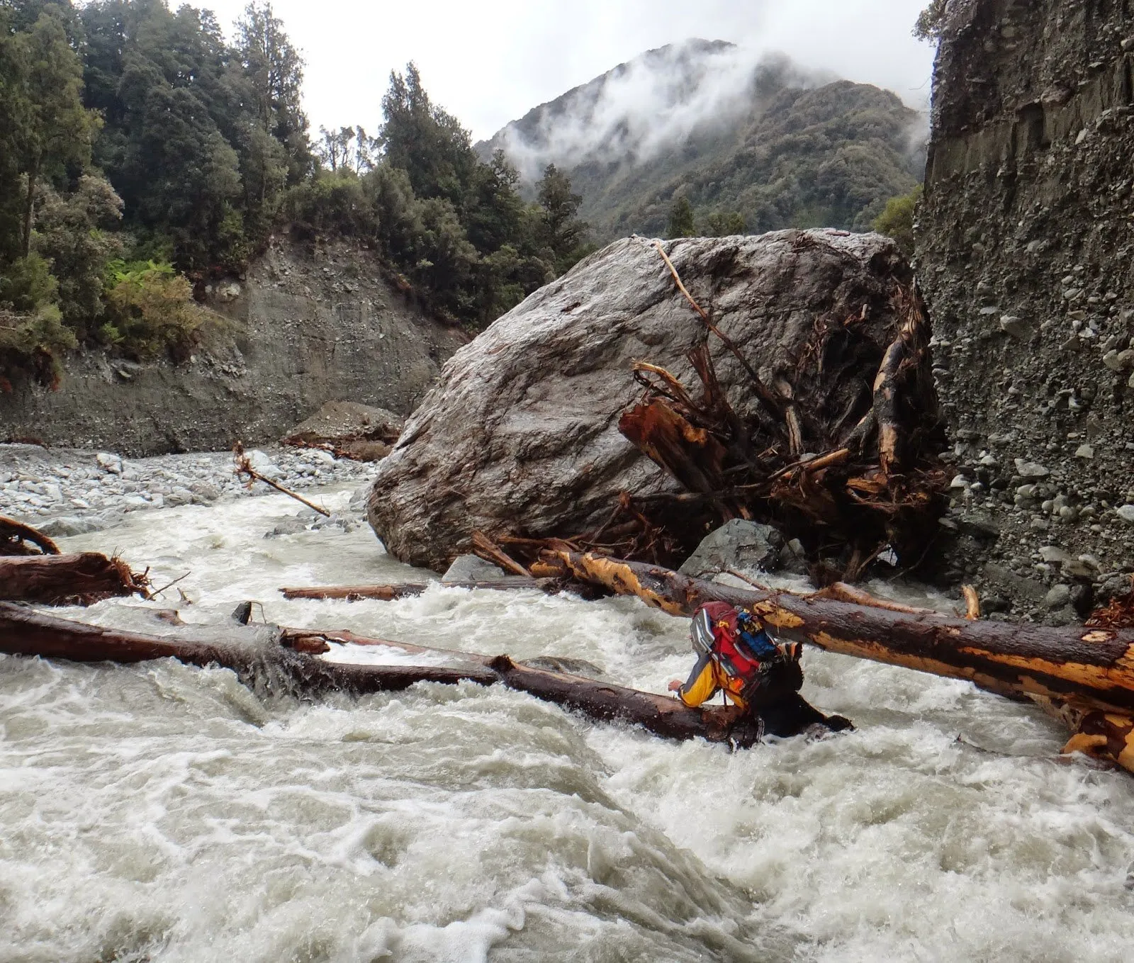 A figure crossing a flooded river below a large boulder
