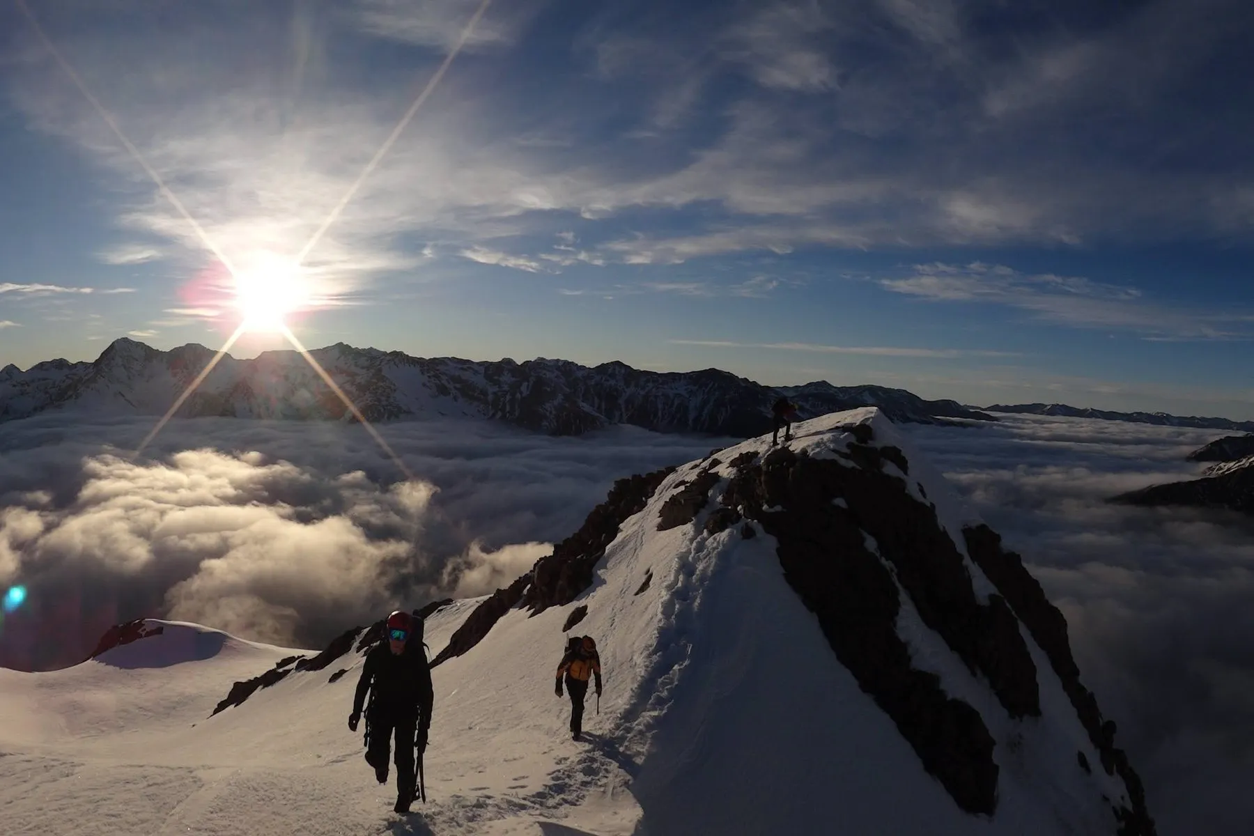Two figures on a snow ridge at dawn, the sun low over cloud