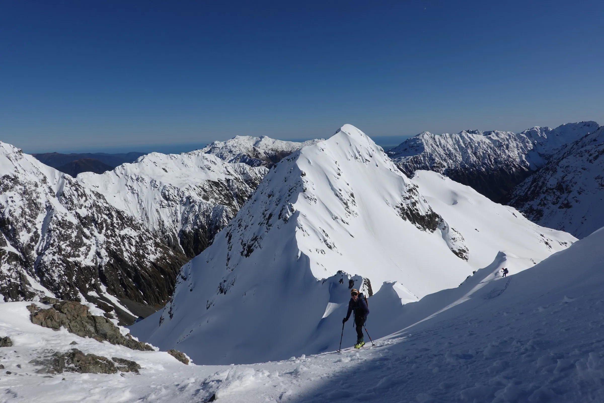 A lone figure on a snow ridge with a wide range of peaks behind